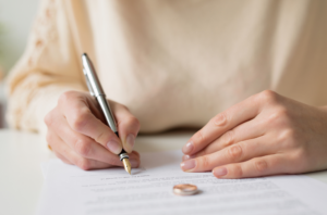 A woman signing divorce papers with a wedding ring on the paper.