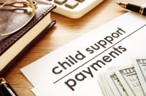 Child support payments paper with money on top of it. A pen, calculator, a book and glasses on a desk.