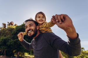 Stepparent holding child on shoulders smiling.