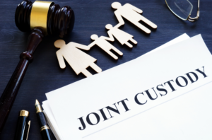 Joint custody paper on a desk next to pens, a gavel, glasses, and a wooden family.